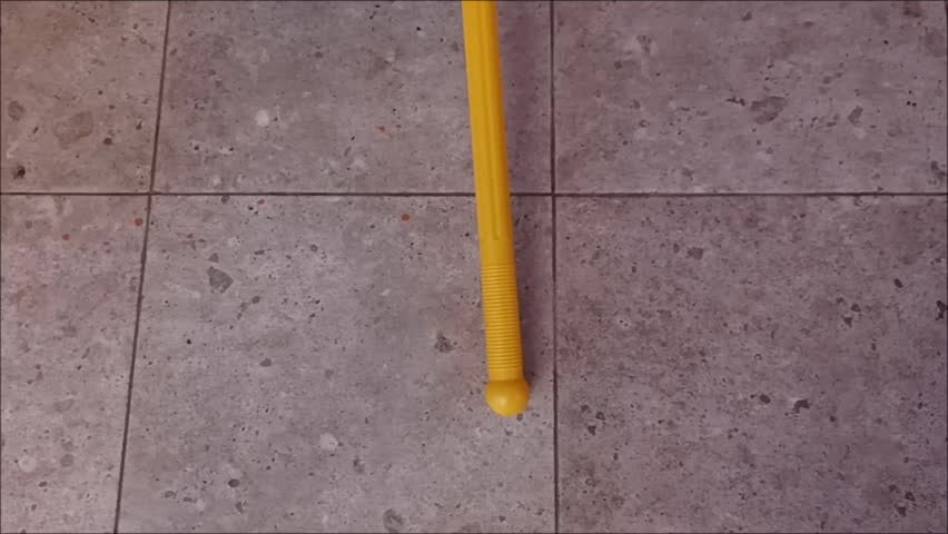 High angle shot of a colorful blue and yellow plastic dustpan on a grey tiled floor for household cleaning chores.