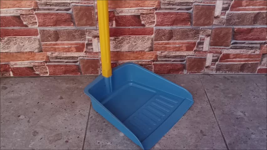 A durable blue plastic dustpan on a tiled floor, perfect for daily indoor and outdoor household cleaning maintenance.