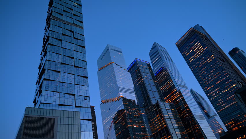 Modern skyscrapers at Hudson Yards New York at dusk. Low angle view of illuminated glass office towers against dark blue evening sky in Manhattan.