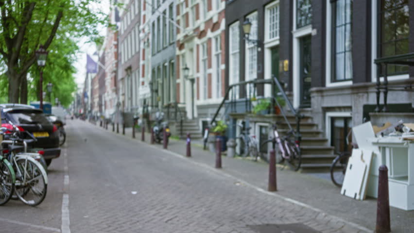 Defocused city street in amsterdam with bicycles parked alongside traditional dutch canal houses and lush green trees creating a serene urban atmosphere outdoors.