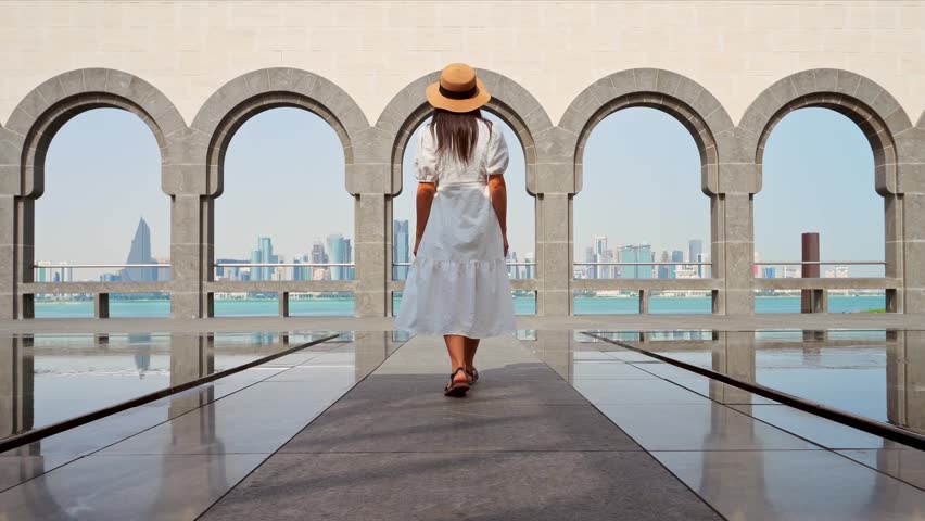 Doha, Qatar - 8th january, 2026: Elegant woman wear white dress walking on famous viewpoint Museum of Islamic Art, Doha. Features iconic stone arches framing modern West Bay skyline and Persian Gulf