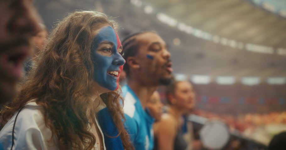 Close-up of a Young Woman With Blue and Red Face Paint Smiling and Chanting Beside a Black Male Supporter, as Happy Football Fans Celebrate a Professional International League Match Game in Stadium.
