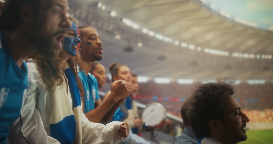 Portrait of Jubilant Soccer Supporters in a Packed Stadium as a Young White Woman With Blue and Red Face Paint Smiles, Shouts and Lifts Her Arms Beside a Black Male Fan During a Major League Cup Match
