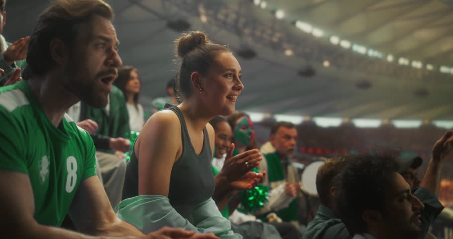 Close-up of a Young White Woman and Mixed Supporters in Green Apparel Celebrating in a Packed stadium Smiling, Shouting and Raising hands During a Professional League Football Cup Match. Slow Motion