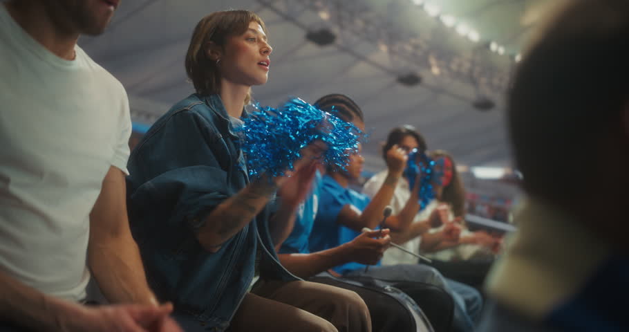 Diverse Soccer Fans Erupt in Championship Excitement Inside a Packed stadium Clapping, Waving Blue Pom-poms and Raising Arms as the Crowd Roars Through a Thrilling Match Atmosphere.
