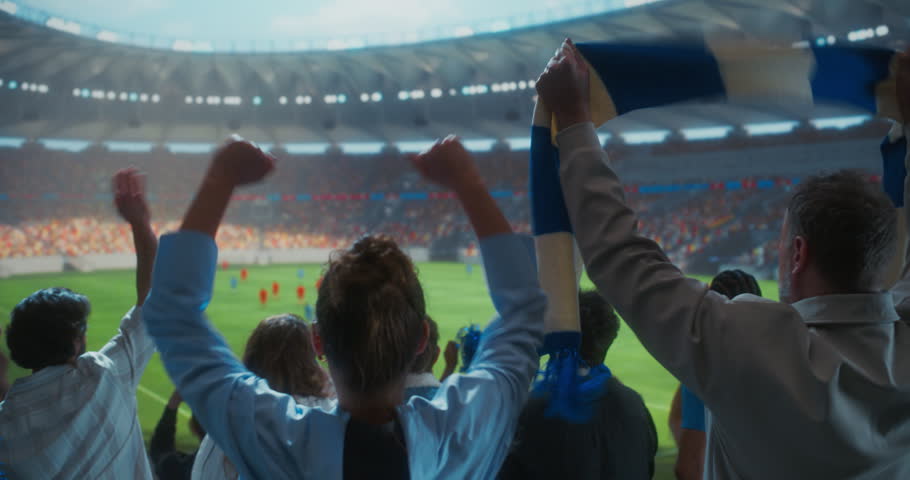 Back-view Soccer Supporters Erupt in Celebration Inside a Packed Stadium, Waving Blue and White Scarves, Clapping and Raising hands as a Professional International Championship Match Unfolds Field