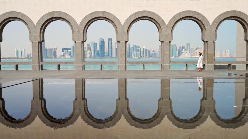 Doha, Qatar - 8th january, 2026: Elegant woman wear white dress walking on famous viewpoint Museum of Islamic Art, Doha. Features iconic stone arches framing modern West Bay skyline and Persian Gulf