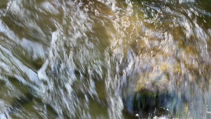 Fast water flow on the stones in the mountain river in sunny day, top view close-up 
