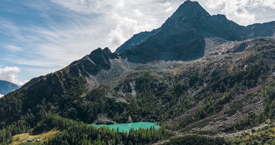 Aerial view showing a clear turquoise lake nestled among rocky mountains and green forests. Hyperlapse