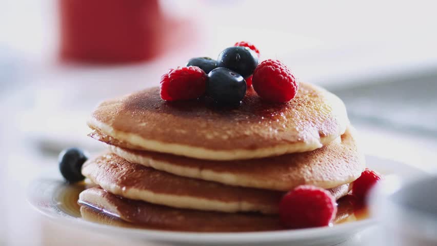 Hands Pouring Maple Syrup Onto a Stack Of Pancakes With fresh berries. pouring syrup onto pancakes applies new mixing of different fruits and berries.