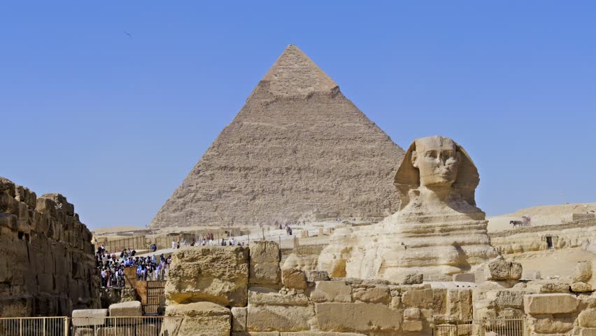 Timelapse of Great Sphinx and Pyramid of Khafre with moving crowds of tourists at Giza plateau, Egypt. Iconic ancient wonder under vivid blue sky. Travel and history content.