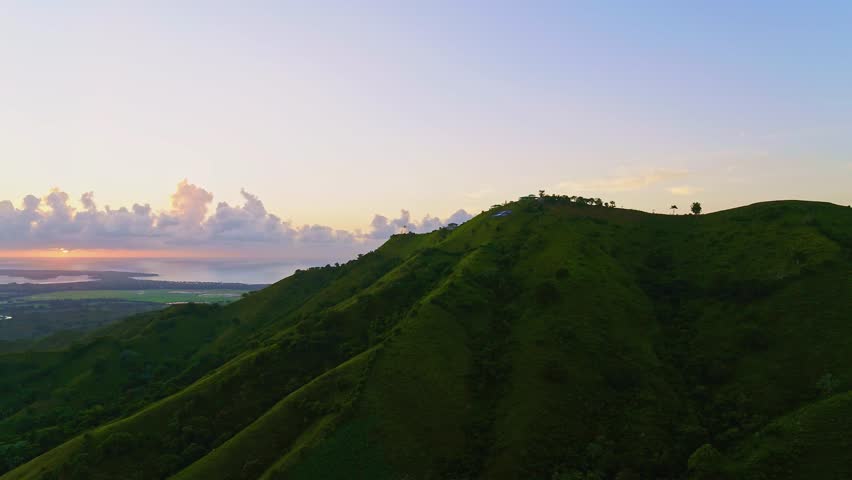 A green mountainside against a backdrop of airy pink clouds in the sunset sky over the ocean. A perfect summer natural landscape. Evening sky over a mountain valley. Sunset in the mountains.