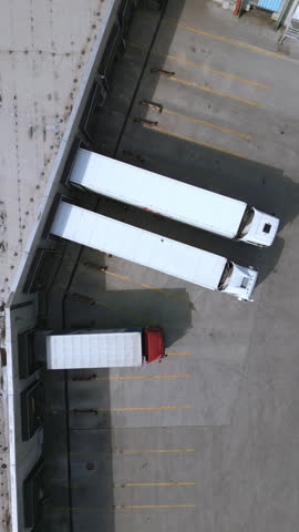 Three trucks are parked in a designated area of a distribution warehouse. The trucks are lined up neatly in the parking lot, ready for freight transportation.