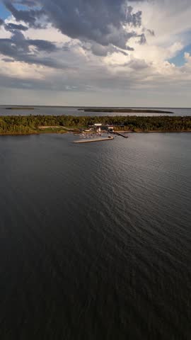 Drone flying forward toward Gull Harbour on Hecla Island Manitoba. Vertical aerial view showing marina, breakwall, boats, island, and shoreline of Lake Winnipeg on a sunny summer day.