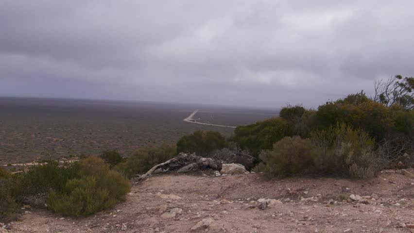 A remote road stretches through a vast desert under a moody cloudy sky.
