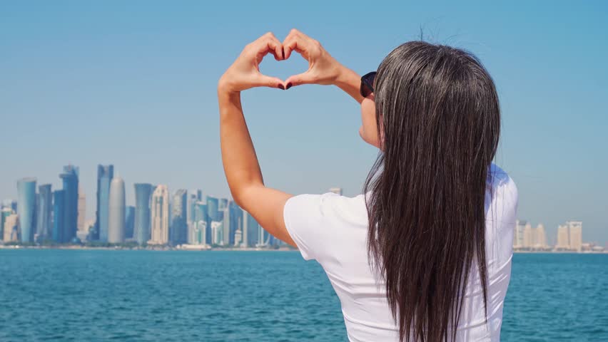 Close up Happy excited young caucasian tourist woman on Doha viewpoint pose make heart enjoy sightseeing Doha city landmarks on Qatar holidays. Travel explore Love Middle east arabic gulf countries