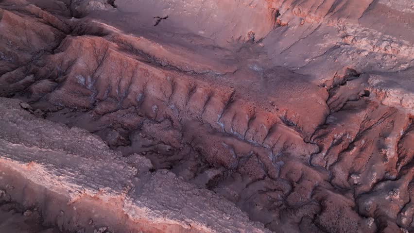 Forward flight over sculpted pink and orange Moon Valley ridges revealing San Pedro de Atacama town nestled in the vast desert plain beyond. San Pedro de Atacama, Chile