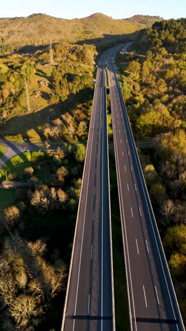 Cars driving on a long highway bridge crossing a lush green valley during a sunny day