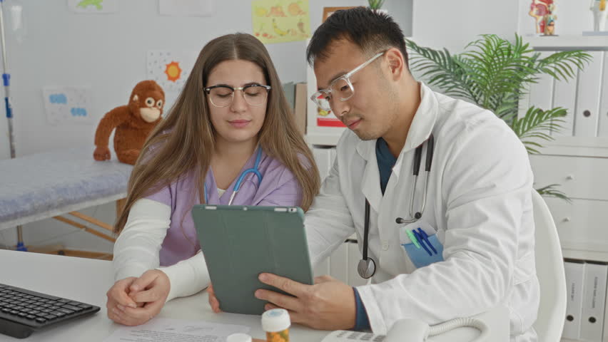 Woman doctor and man doctor holding a tablet and smiling in a medical clinic building with stethoscope and pill bottles visible; reassurance teamwork consultation.