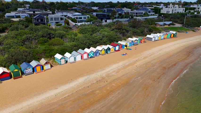 Aerial drone view of Brighton Beach, Port Phillip Bay, Melbourne, Victoria. Colorful Brighton Bathing Boxes along the beach. Tourists walking on the sand near wooden beach huts.	