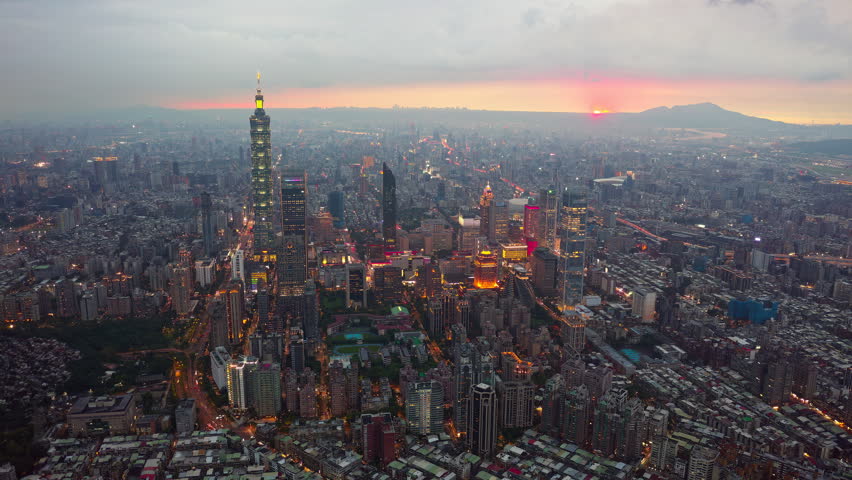 Aerial hyperlapse footage from dusk till night above Downtown Taipei, an international metopolis and the vibrant capital city of Taiwan, with 101 Tower standing out amid modern skyscrapers in XinYi Commercial District and city lights dazzling under dramatic twilight sky.