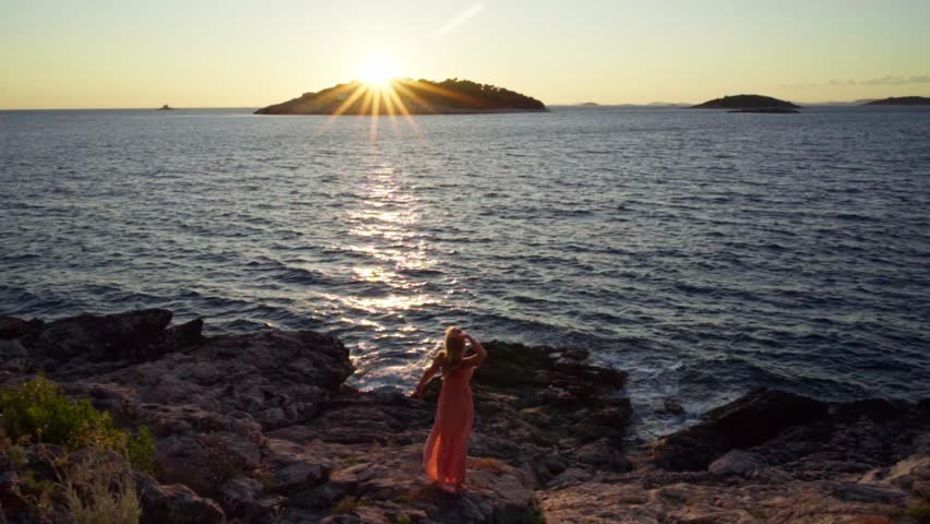 Blonde woman in summer dress walking outdoors in nature close the sea in Croatia at sunset. Beautiful evening at sunset.