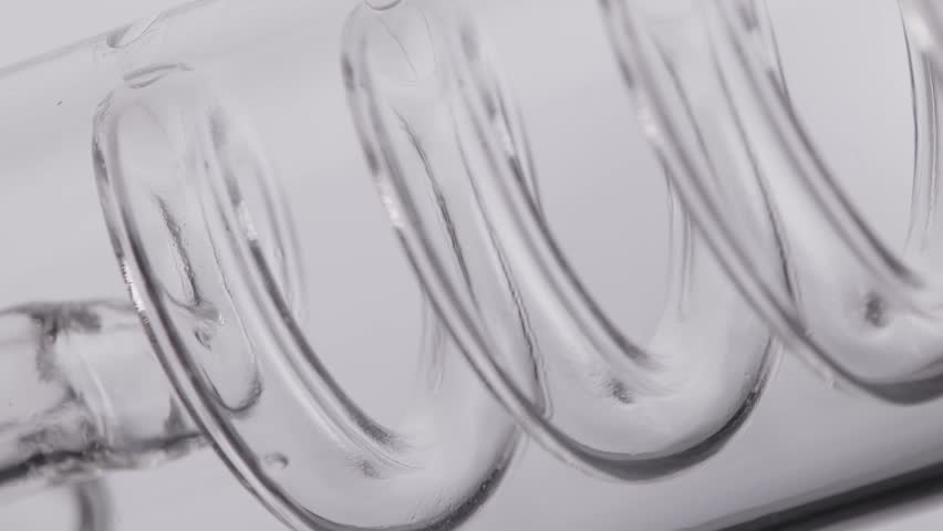 Concept craft drink coffee industry. Glass spiral coil containing amber liquid in tube on white background.