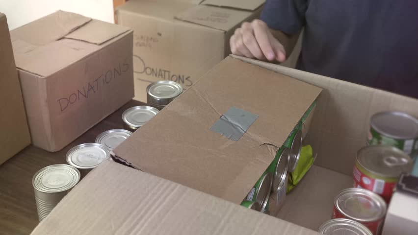 Man Preparing Box Of Donations at home putting canned foodin boxes