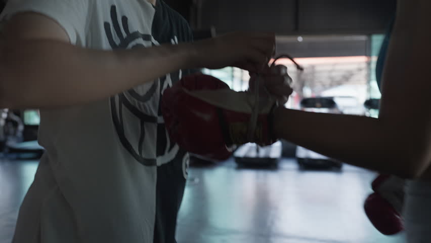 Two people wrap boxing gloves in a gym. Hands work together to secure the gear. Focus on close-up details of the process