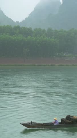 Vertical screen River Boat Asian Fisherman Phong Nha Vietnam Misty Karst Backdrop, Solitary Boat Laden With Woven Cargo Sacks Gliding Across Pale Green Water, Low Fog Hugging Forested