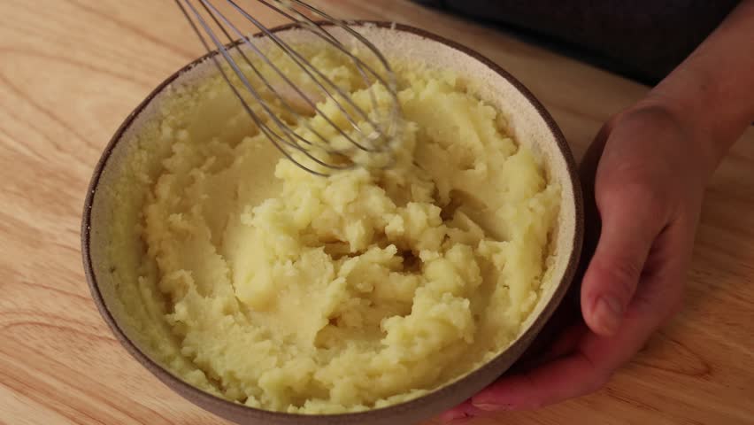 Mixing mashed potatoes in bowl while adding liquid for creamy texture.