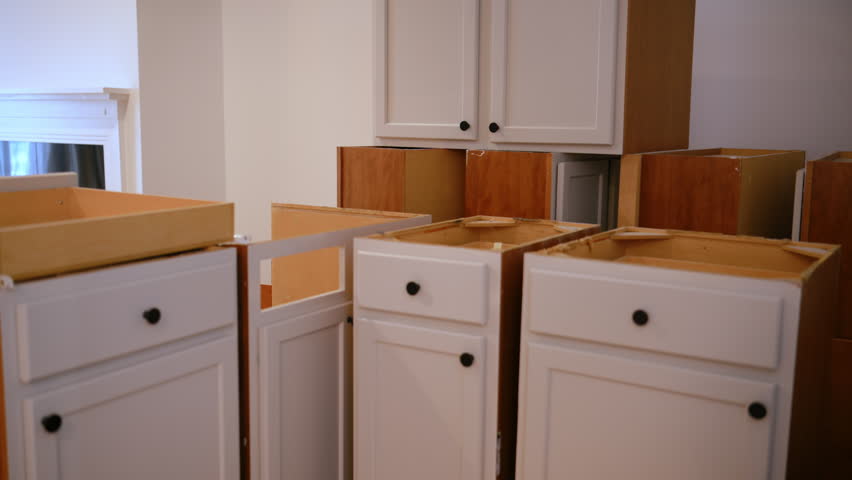 Kitchen cabinets partially disassembled during home renovation. White cabinet frames with removed countertops and exposed interiors.