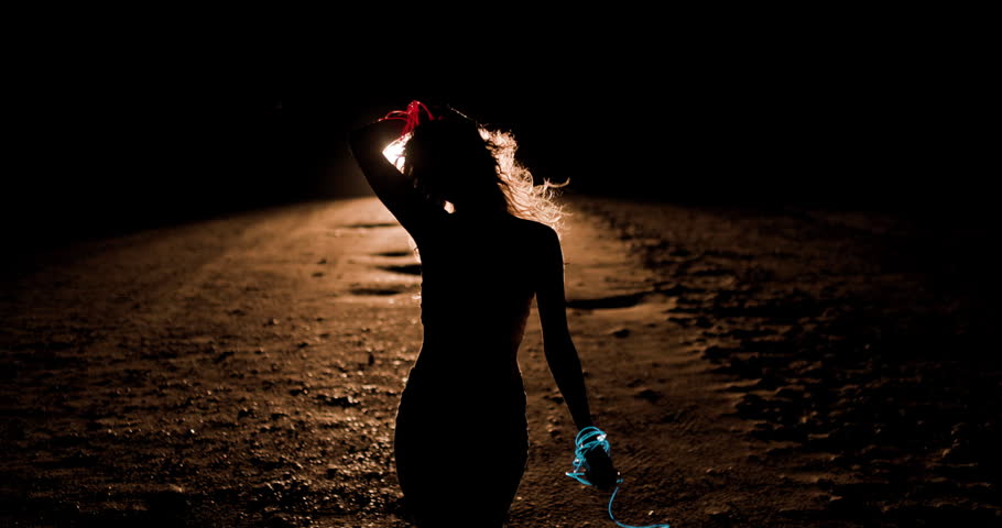 A girl creating beautiful movements against the backdrop of car headlights on a deserted road at night. The light casts an enchanting silhouette, highlighting her graceful dance.