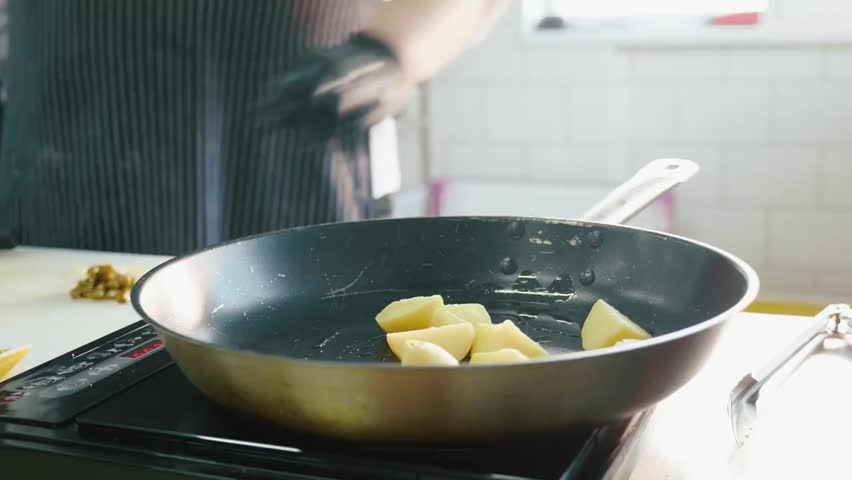 Professional chef stirring and tossing chopped potatoes in a frying pan close-up, showcasing cooking process, sizzling food, and culinary skills.