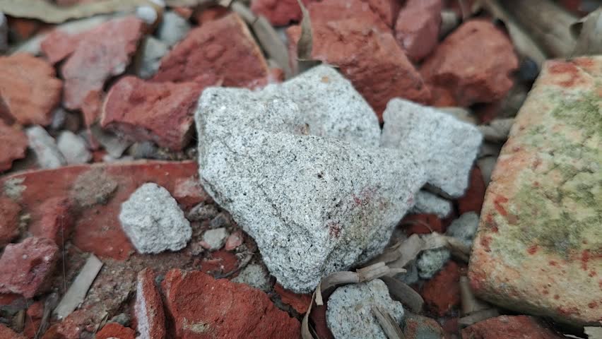 A close up view of a rough grey stone resting on a bed of broken red bricks in a garden setting.