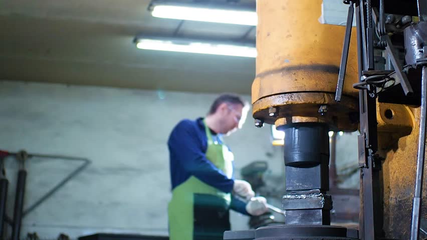 Blacksmith hammering hot iron automatic hammer. Blacksmith uses a hydraulic hammer to forge hot metal in his workshop.