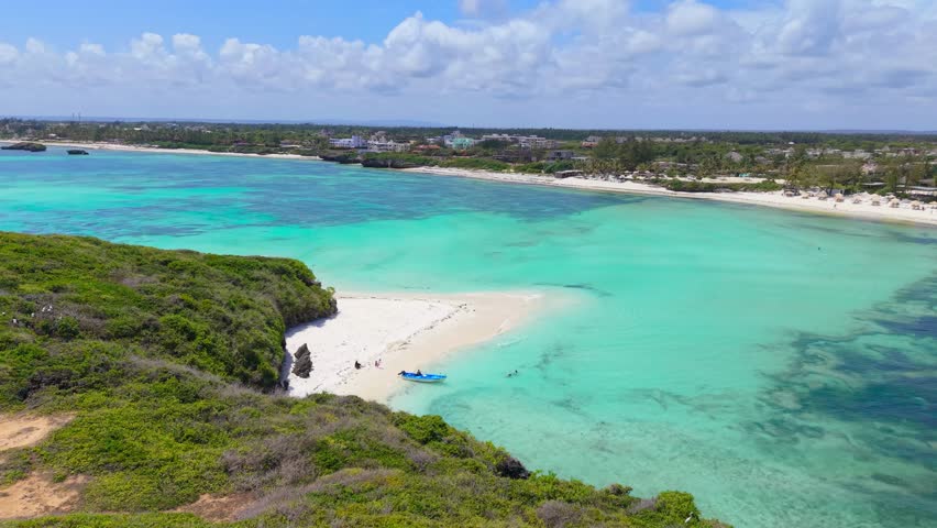 Aerial view of turquoise ocean water and white sandbanks surrounded by green coastal cliffs and village buildings at Watamu Beach, Kenya.