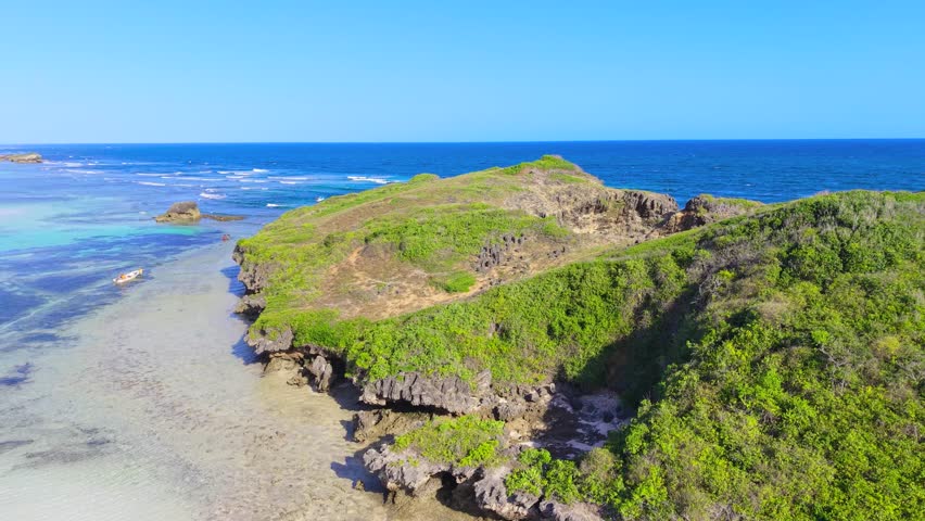 Aerial view of rocky cliffs covered in green vegetation overlooking the turquoise Indian Ocean with a boat at Watamu Beach, Kenya.