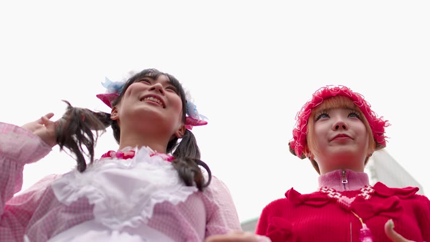Two women wearing vibrant pink decora street style fashion laugh together at Shibuya Crossing Tokyo