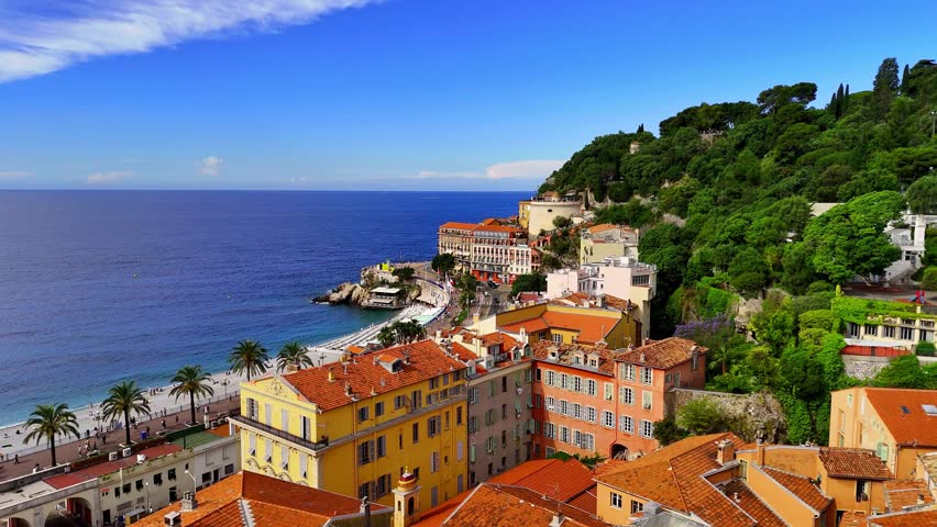 Aerial view of Nice, France, with colorful old town rooftops, Castle Hill, palm-lined beach, and the sparkling Mediterranean along the French Riviera coastline.
