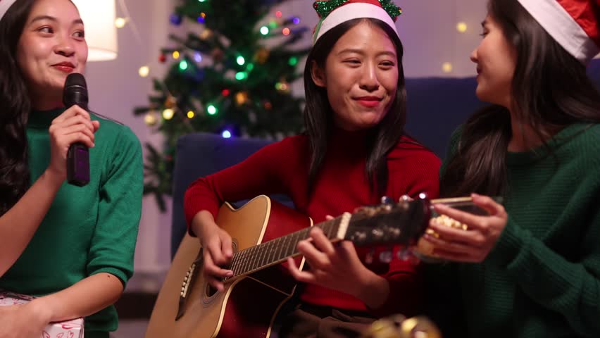 Asian woman singing Christmas carols at home party. Three asian women wearing santa hats are having a Christmas party at home.