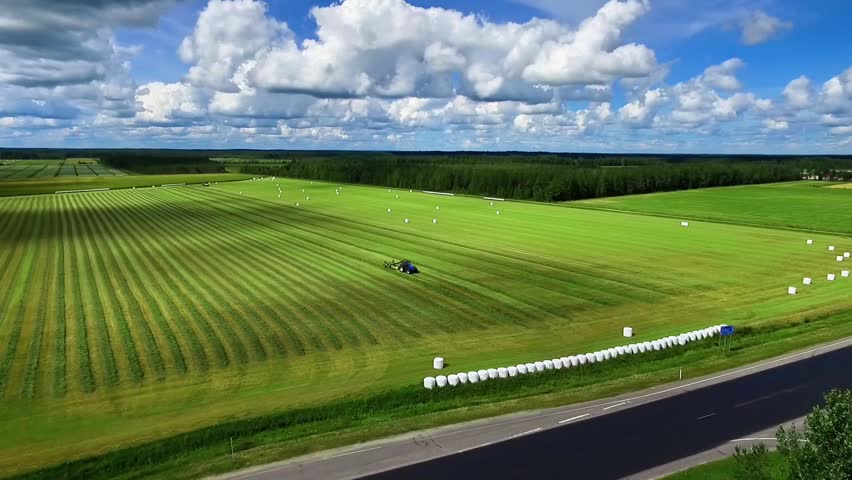 Expansive Green Fields Under a Bright Sky: Harvesting With Machinery in Scenic Landscape in Finland