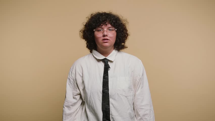 A person stands in a studio with a yellow background. They alternate between different expressions and gestures while wearing a white shirt and black tie. The actions seem playful.