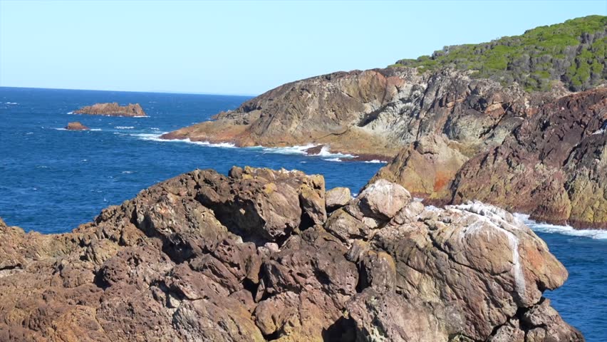 Rocky headland in foreground with coastal cliffs and ocean beyond, Tathra, New South Wales, Australia.