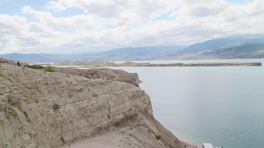 Cliff Overlooking Calm Lake Under Cloudy Sky, Distant Hills, Soft Light, Summer Atmosphere. Media