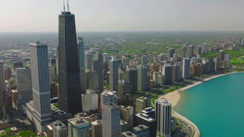 Drone aerial of Chicago’s Near North Side lakefront with 875 N. Michigan Avenue, Lake Shore Drive, and Lake Michigan in view. Bright daytime skyline scene with turquoise water and boats.