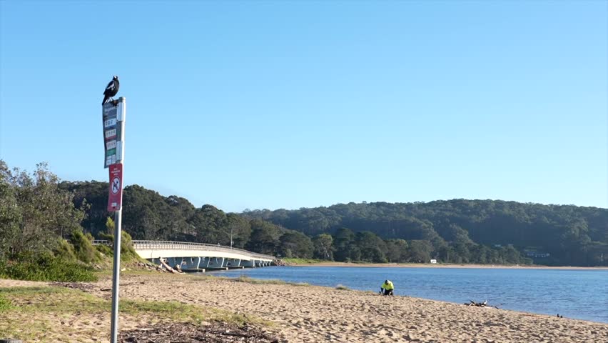 Sandy beach with coastal bridge and signpost in foreground, Tathra, New South Wales, Australia.
