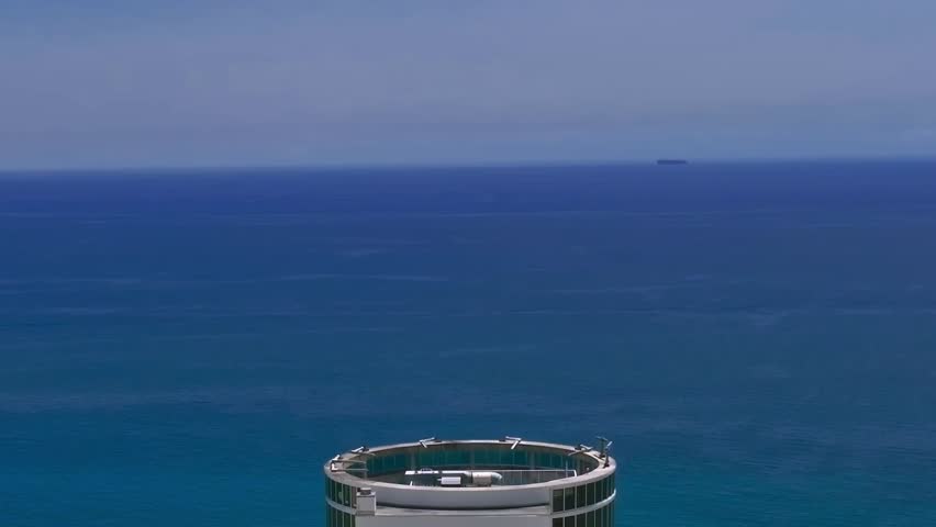 The scene shows the coastline of Miami with buildings near the shore. Calm ocean waters stretch out in the background. A ship can be seen sailing in the distance.