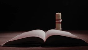 A hand with a match lights a beeswax candle, casting a warm, flickering glow over an open book on a wooden table. Concept of seeking knowledge, tradition, or finding hope in darkness. - Powered by Shutterstock - Get 15% off with code: PIKWIZARD15
