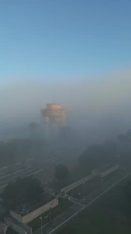  Vertical aerial view of the White Tower of Thessaloniki emerging from thick morning fog.